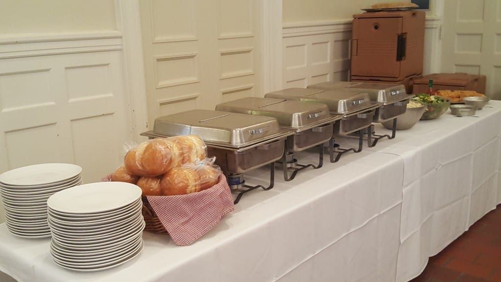Buffet line with chafing dishes, bread rolls and stacked plates