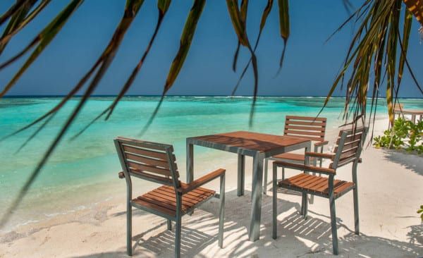 Wooden dining table and chairs on the sand beside the sea