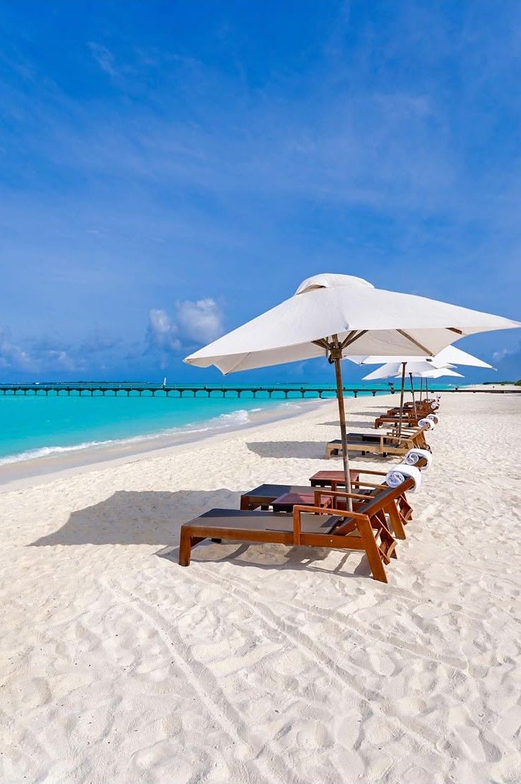 Timber sun loungers under white umbrellas on a white-sand beach beside a turquoise lagoon