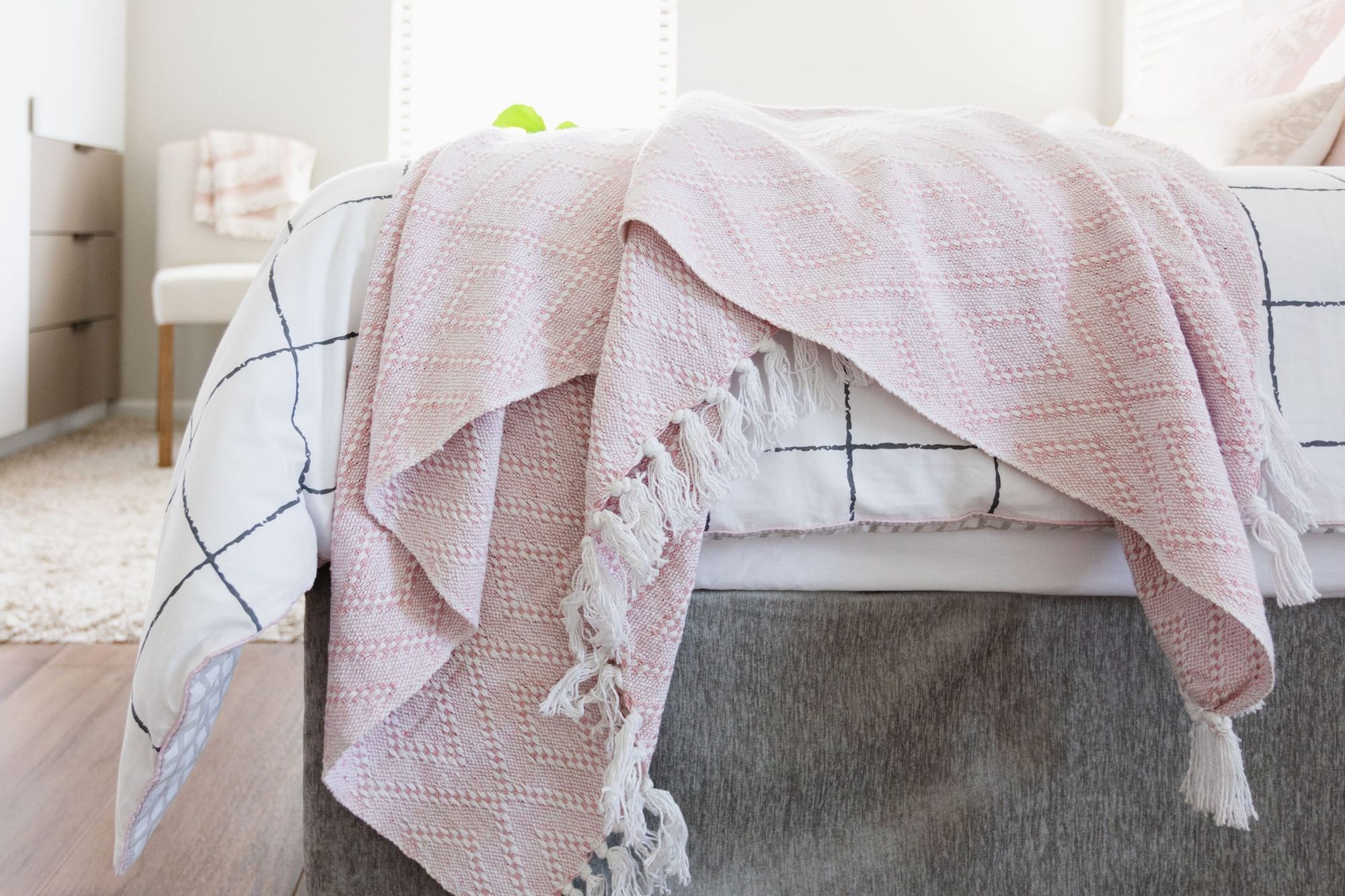Made-up bed with a folded pink throw and cushions