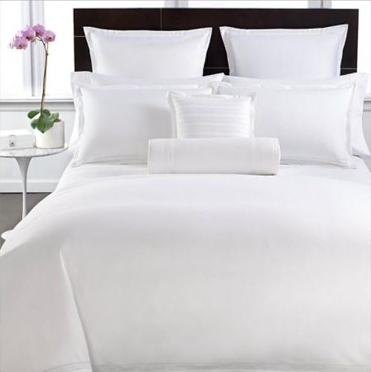 Hotel bed dressed in white linen with layered pillows and an orchid on the side table