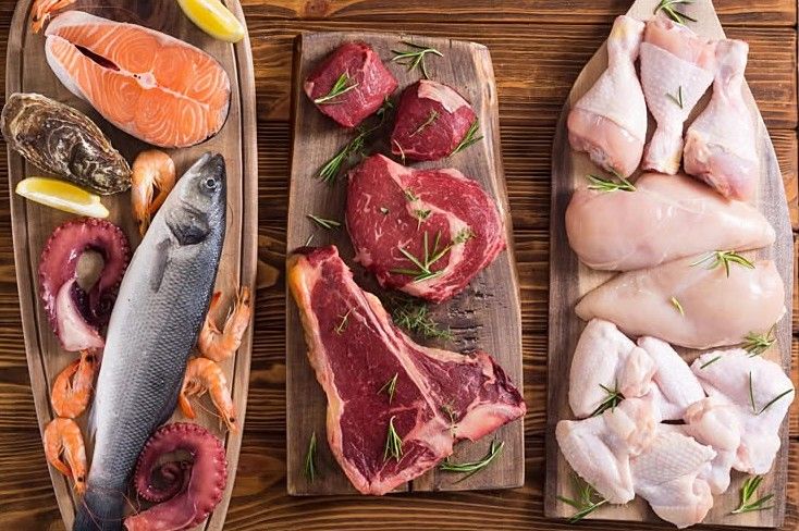 Salmon, whole fish and octopus, beef steaks and chicken laid out on timber boards