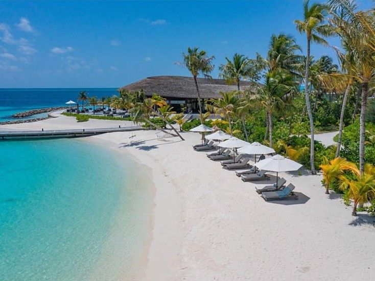 Resort beach with sun loungers and umbrellas under palms beside a turquoise lagoon