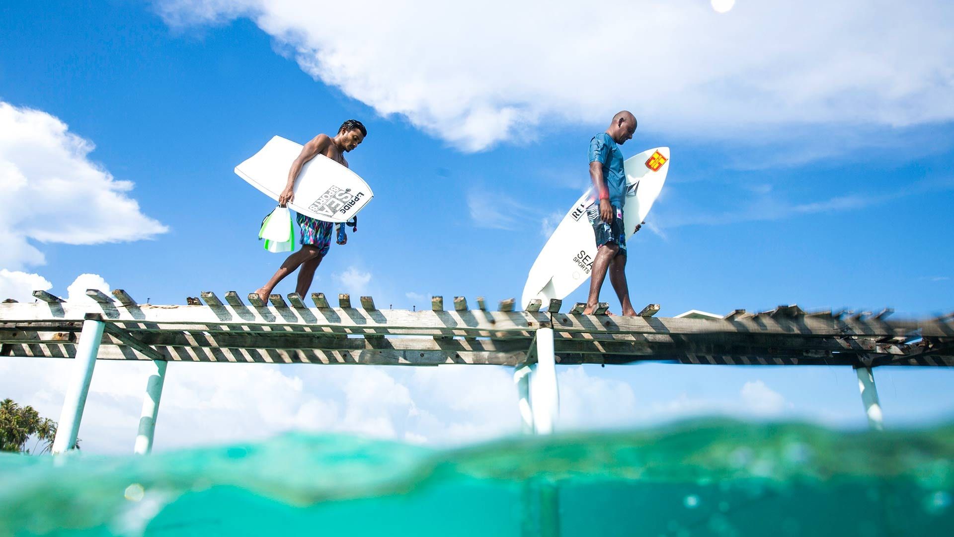 Two surfers carrying boards along a jetty